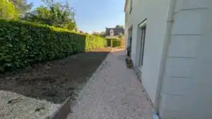 Allée gravillonnée longeant la maison et massif remis au niveau de l’allée, le long d’une haie
