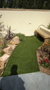 Allée en gazon synthétique bordée d’un massif planté de rochers et de graminées