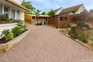Allée gravillonnée bordée de jardinières en bois menant aux abris de jardin en bois