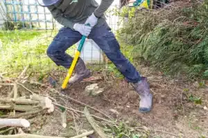 Jardinier dessouchant à la barre à mine, branches coupées au sol, à Buc