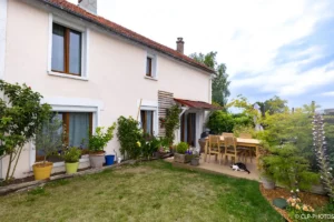 Façade de maison côté jardin avec terrasse et massifs
