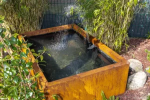 Fontaine à eau dans un bassin en acier corten entourée de bambous et de galets
