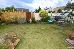 Jardin avec pelouse, serre, palissade en bois et massifs fleuris