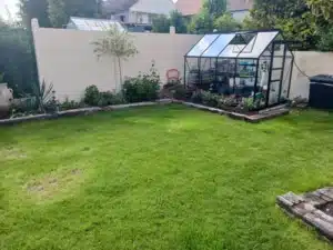 Jardin avec pelouse, serre et massifs bordés de traverses