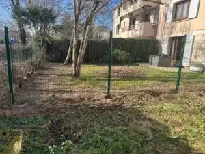 Jardin terre à nu fermé par un grillage rigide vert, résidence au fond, à Buc