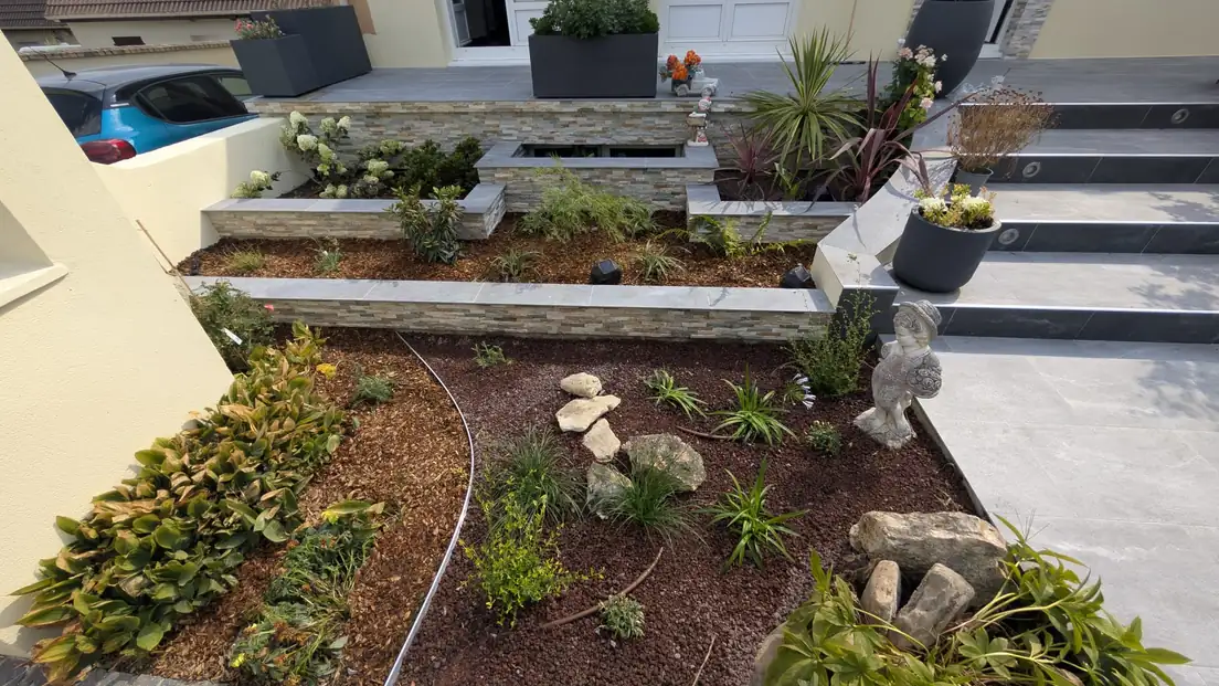 Massifs paillés réaménagés avec rochers et plantations au pied d’une terrasse