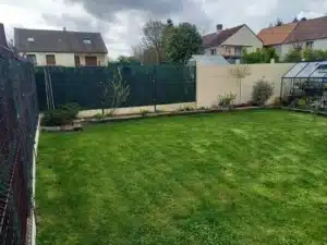 Pelouse entourée de massifs plantés et d’une clôture
